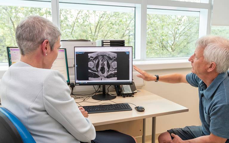 A doctor shows a white-haired man a scan on her computer